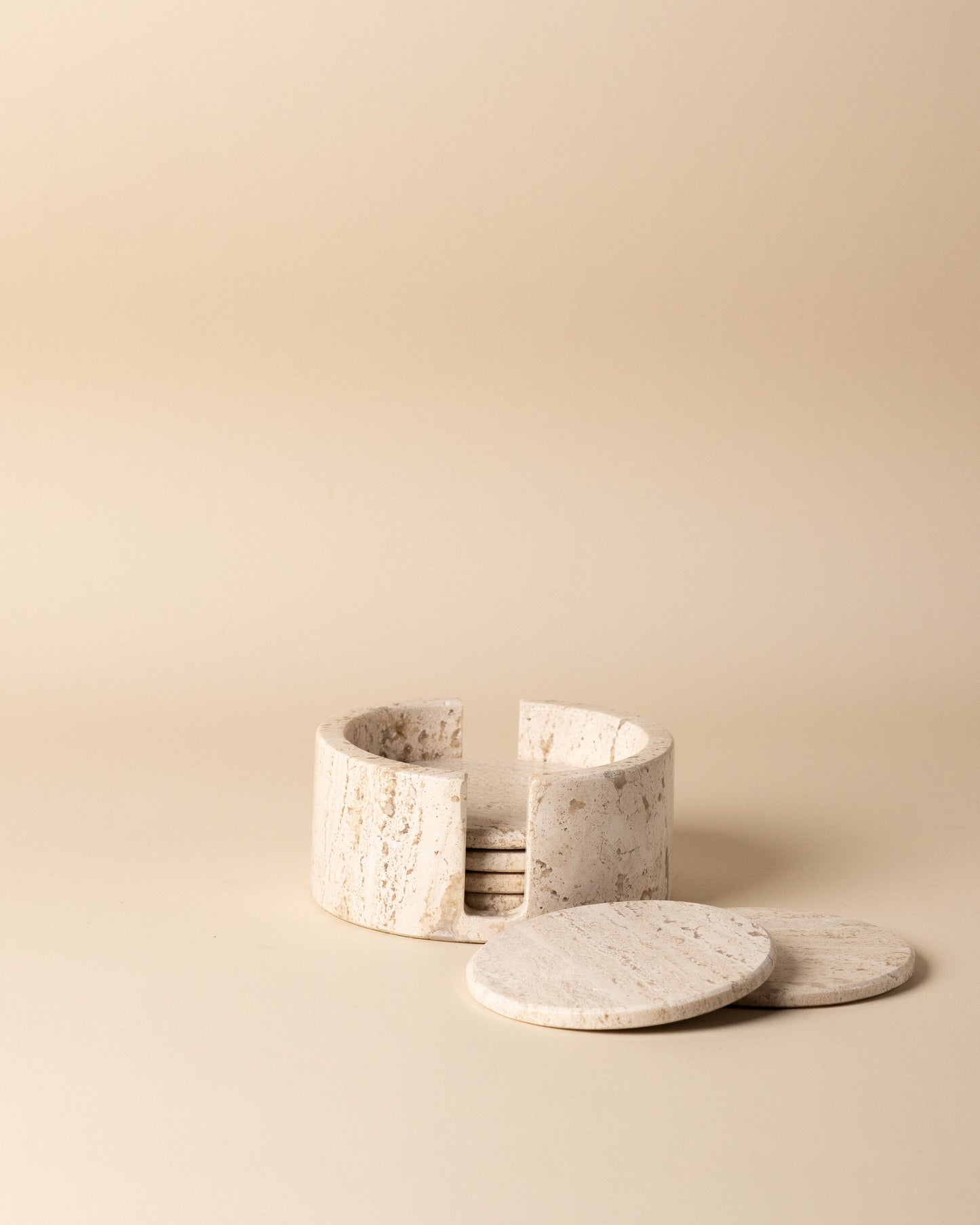 Set of travertine marble coasters with a holder on a beige background