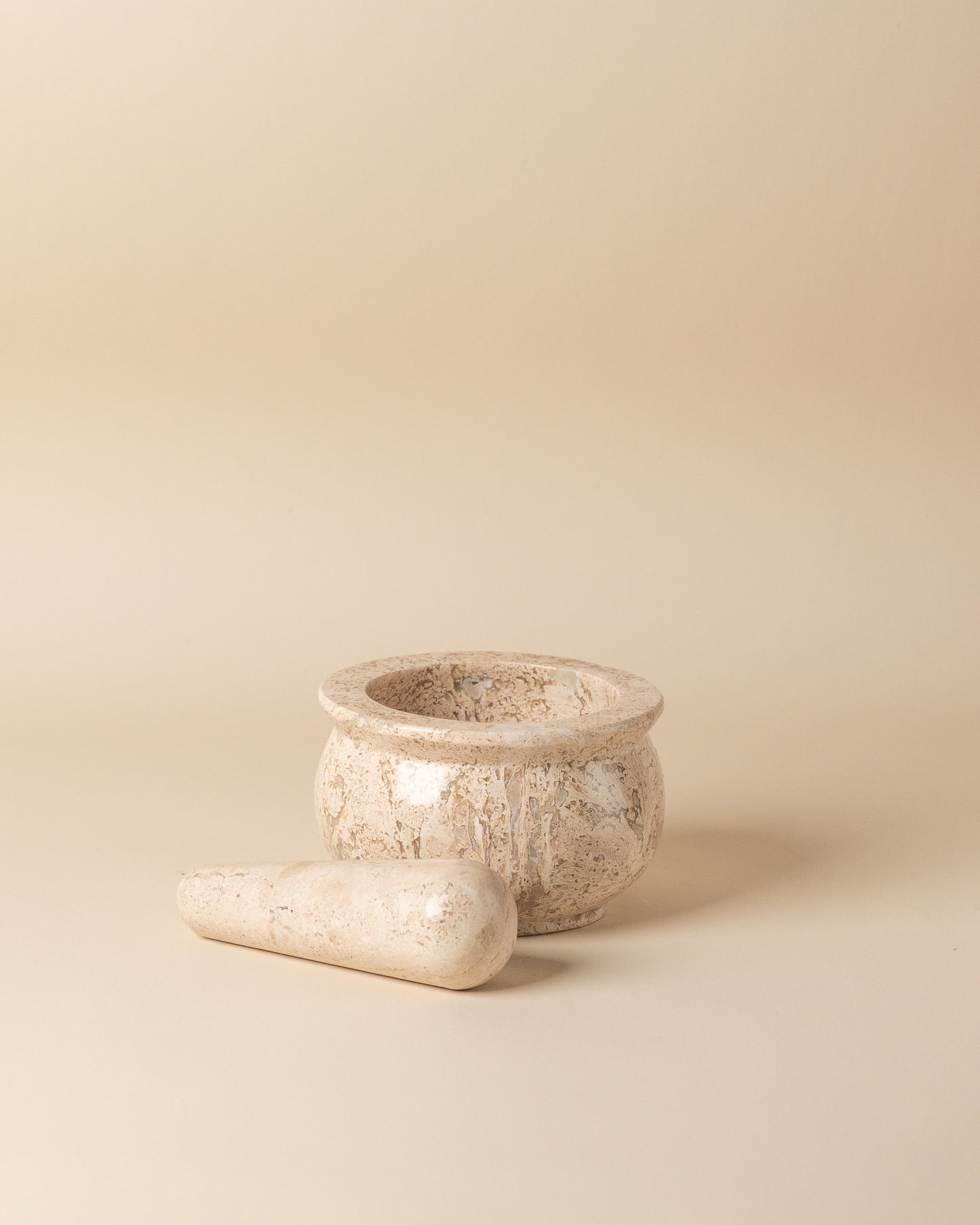 Travertine mortar and pestle set on a beige background