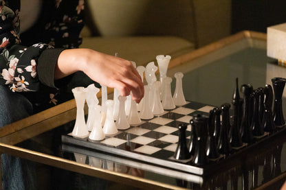 Stimmungsvolles Lifestyle-Bild des Marmonix Schachspiels, bei dem eine Mädchen den ersten Zug mit einer weißen Onyx-Figur macht, um die Exklusivität und edle Haptik des Sets im Gebrauch zu zeigen.