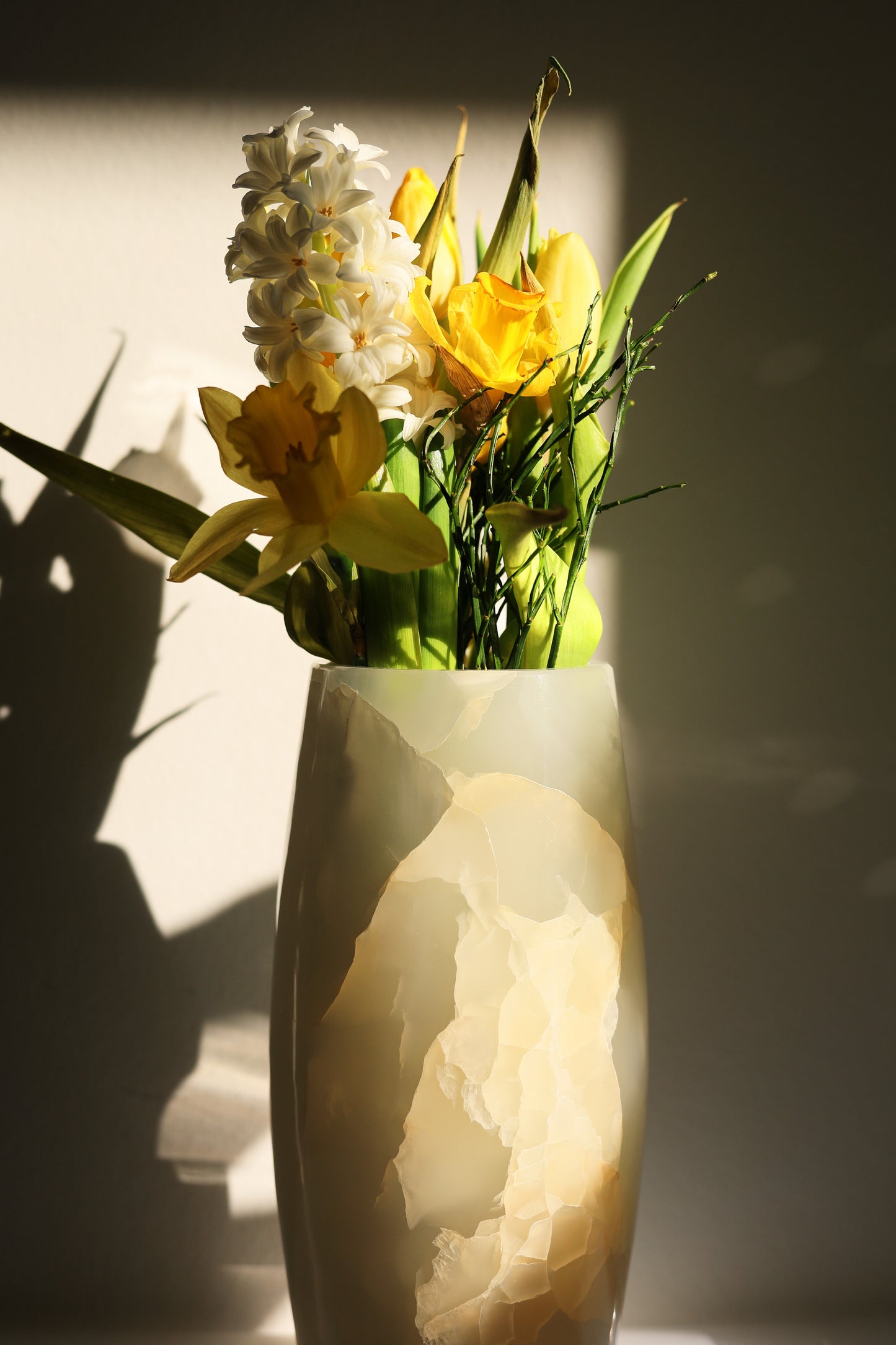 Die prachtvolle weiße Onyxvase von Marmonix, elegant mit frischen Blumen arrangiert in einem lichtdurchfluteten Eingangsbereich.