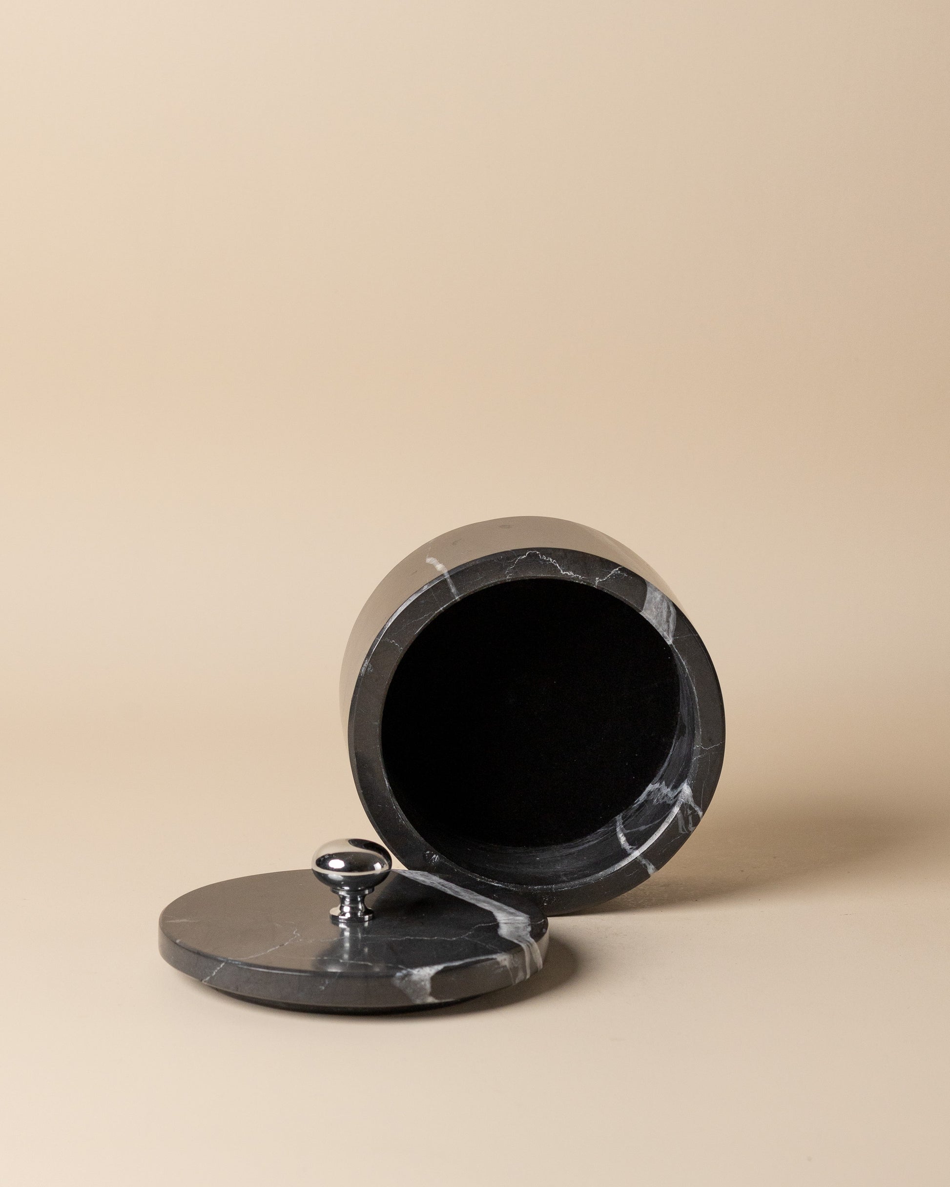 Black marble container with a lid on a beige background