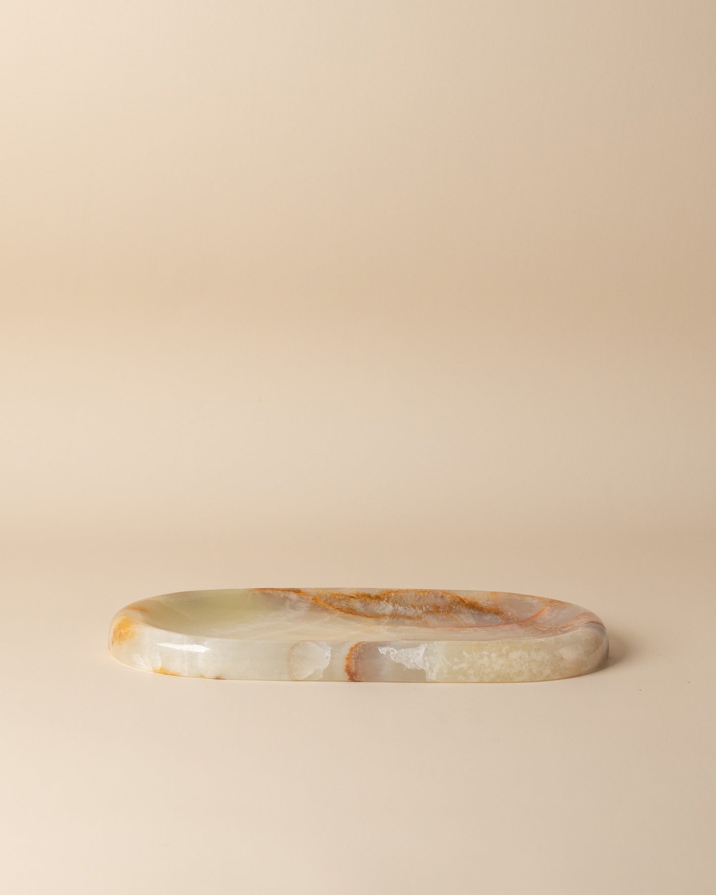 Oval stone tray with onyx translucent green and brown patterns on a beige background