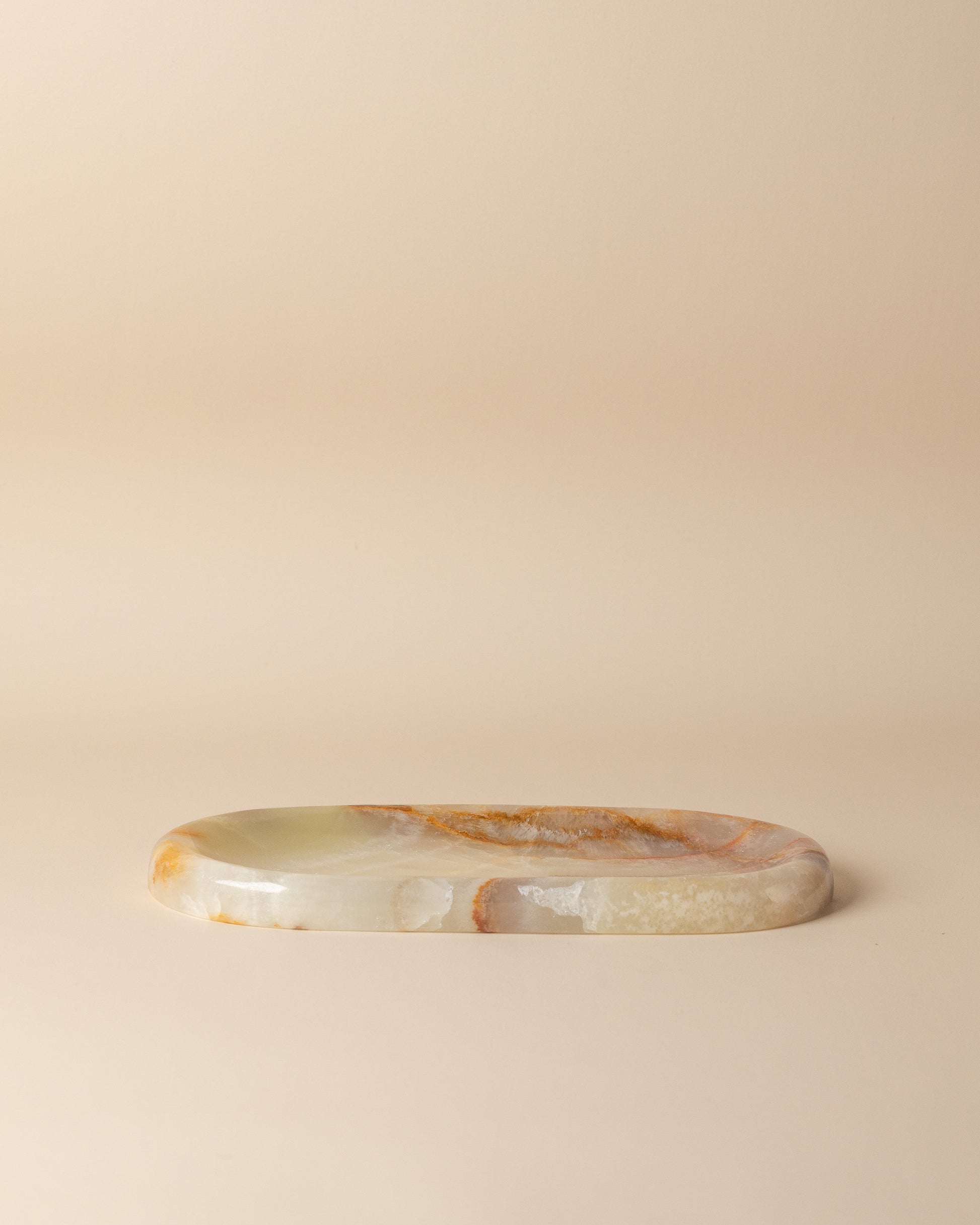 Oval stone tray with onyx translucent green and brown patterns on a beige background
