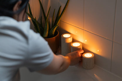 Luxuriöse Spa-Ambiente-Aufnahme im Badezimmer, bei der das dreiteilige Travertin-Teelichthalter-Set von Marmonix stimmungsvoll am Rand einer Badewanne angezündet wird, um eine entspannende Wellness-Atmosphäre zu kreieren.