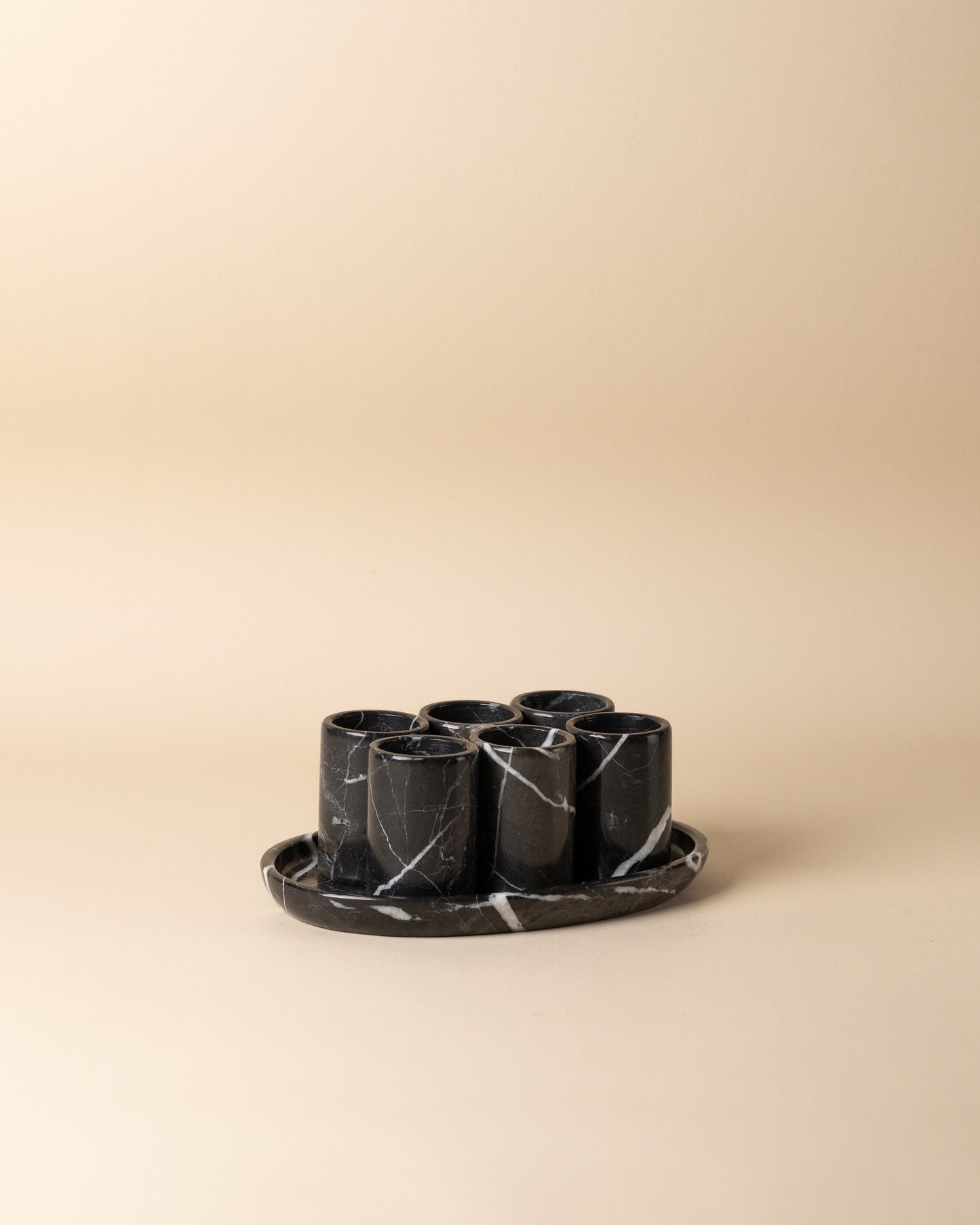 Set of six black marble cups with a tray on a beige background