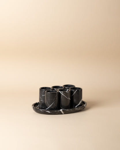 Set of six black marble cups with a tray on a beige background