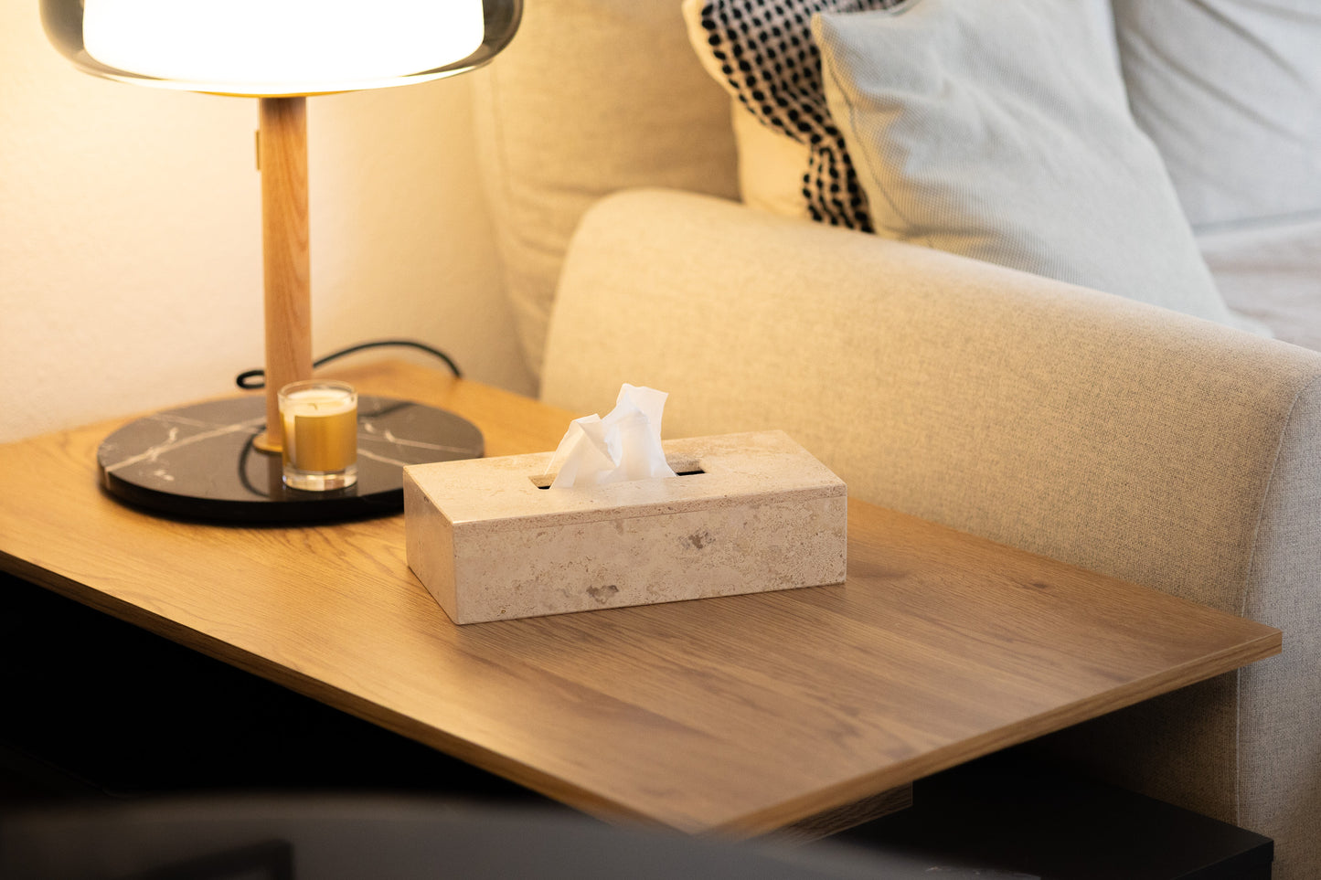 Die luxuriöse Kosmetiktuchbox-Abdeckung aus Travertin von Marmonix, stilvoll inszeniert auf einem Nachttisch neben einer Lampe für ein gemütliches und exklusives Wohnzimmer-Ambiente.